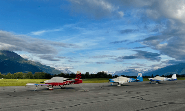 Three small airplanes parked on a runway with mountains and a blue sky in the background.